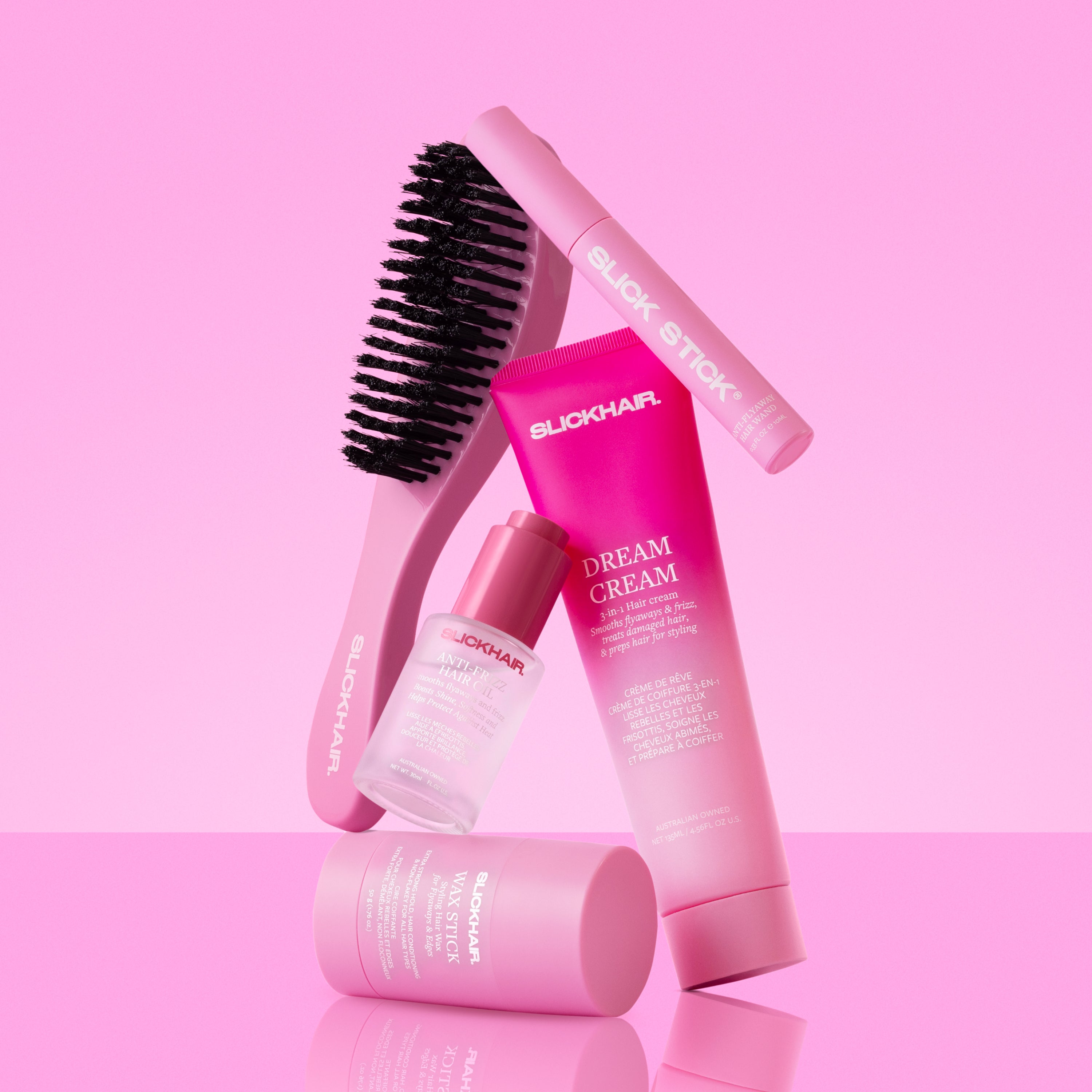 SLICKHAIR product set including a pink hair brush, SLICKHAIR Dream Cream, slick stick anti-flyaway hair wand, wax stick and anti-frizz hair oil on a pink background.