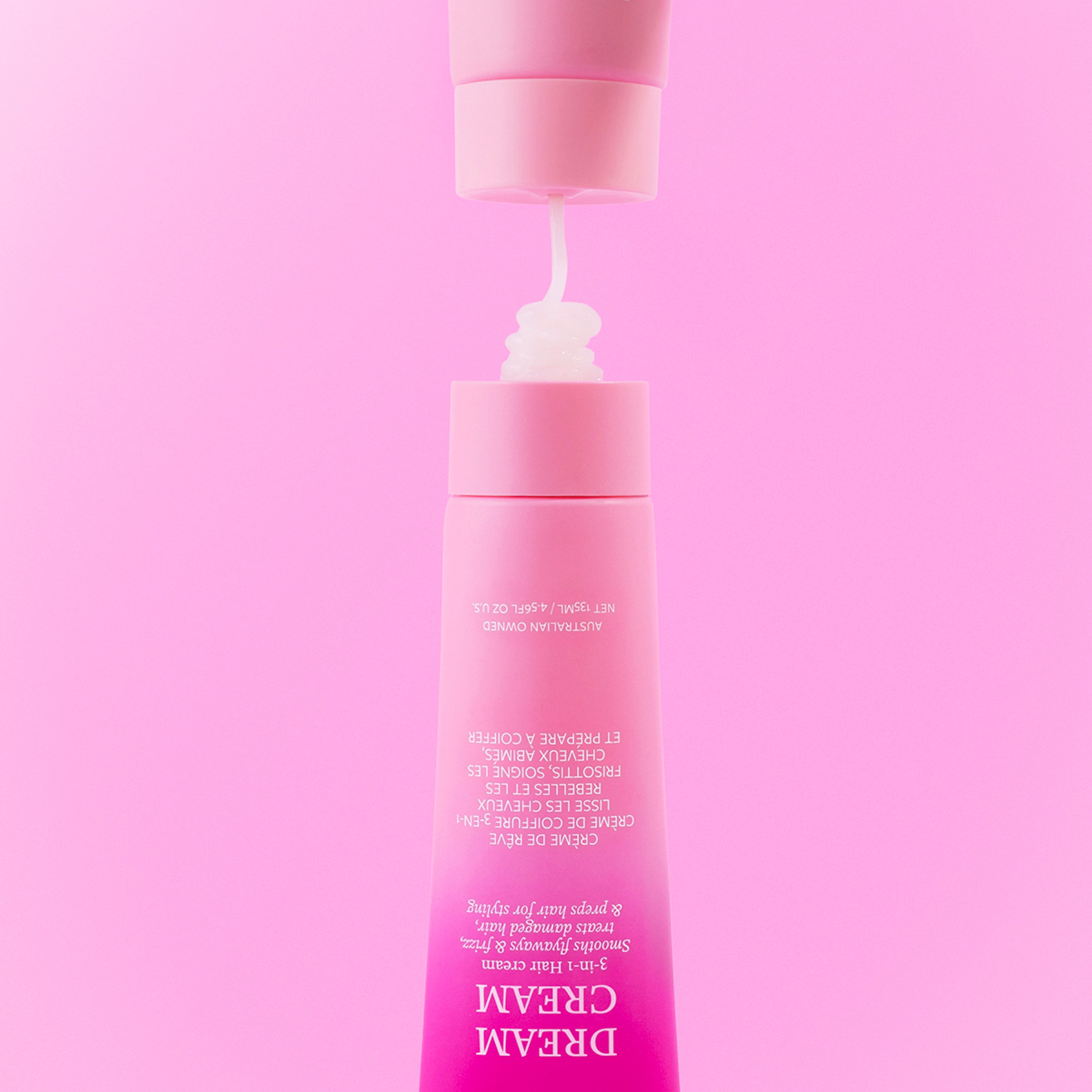 Upside down pink tube of SLICKHAIR Dream Cream on a pink background