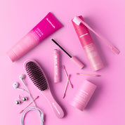 Pink SLICKHAIR hair products including a hair brush, dream cream, wax stick, anti-flyaway gel dup and slick stick hair wand on a pink background.